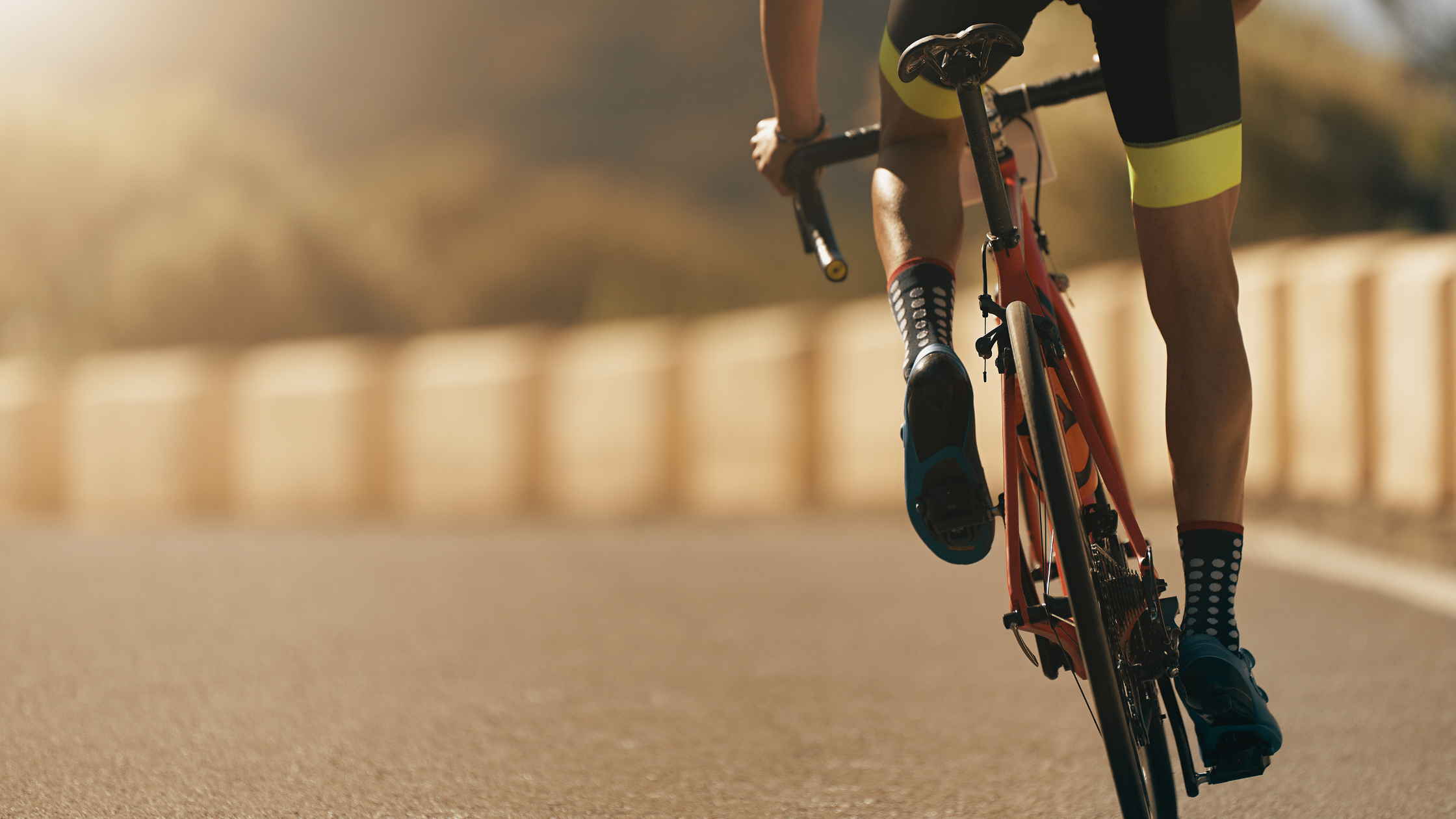 Image shows a road cyclist on an empty road heading towards the sun