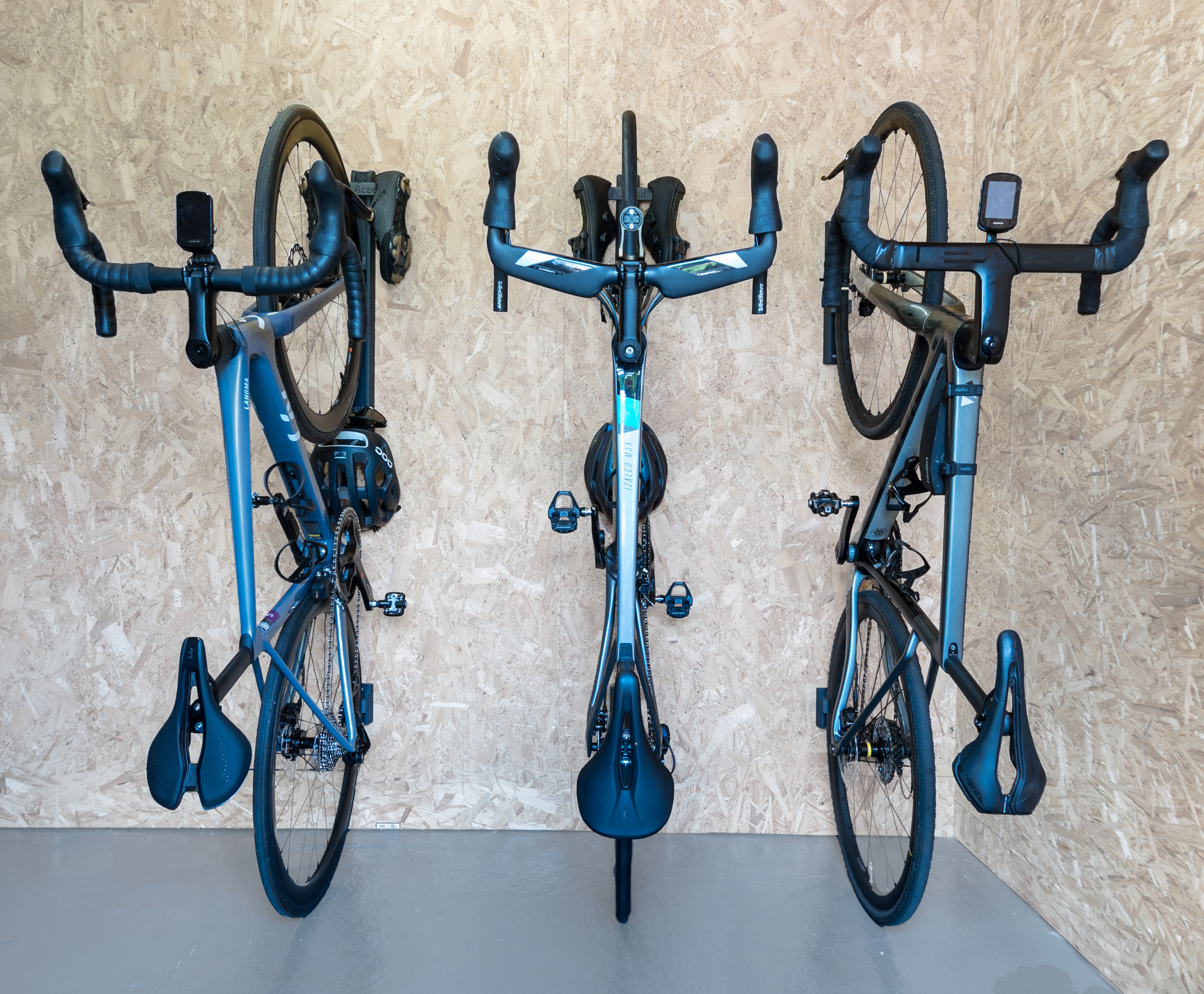 Three bikes lined up and stored vertically using the PLAced rail system. Two bikes use the extended rails which are holding the riders helmets, sunglasses and cleats.