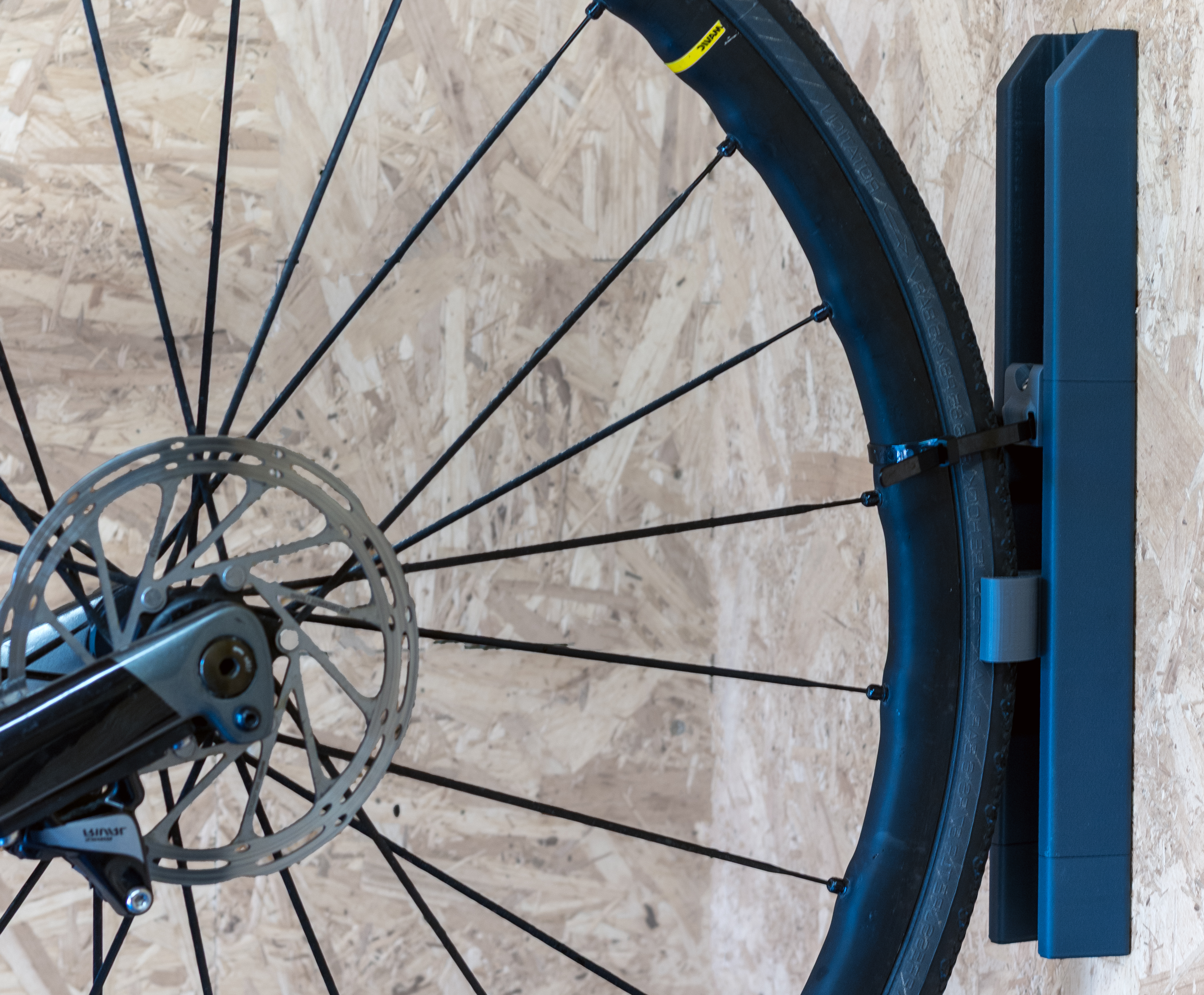 Close up shot of a road bike wheel stored in the PLAced standard uprlight rail kit - the Verticale. The bike has been secured for winter storafge with a reusable cable tie